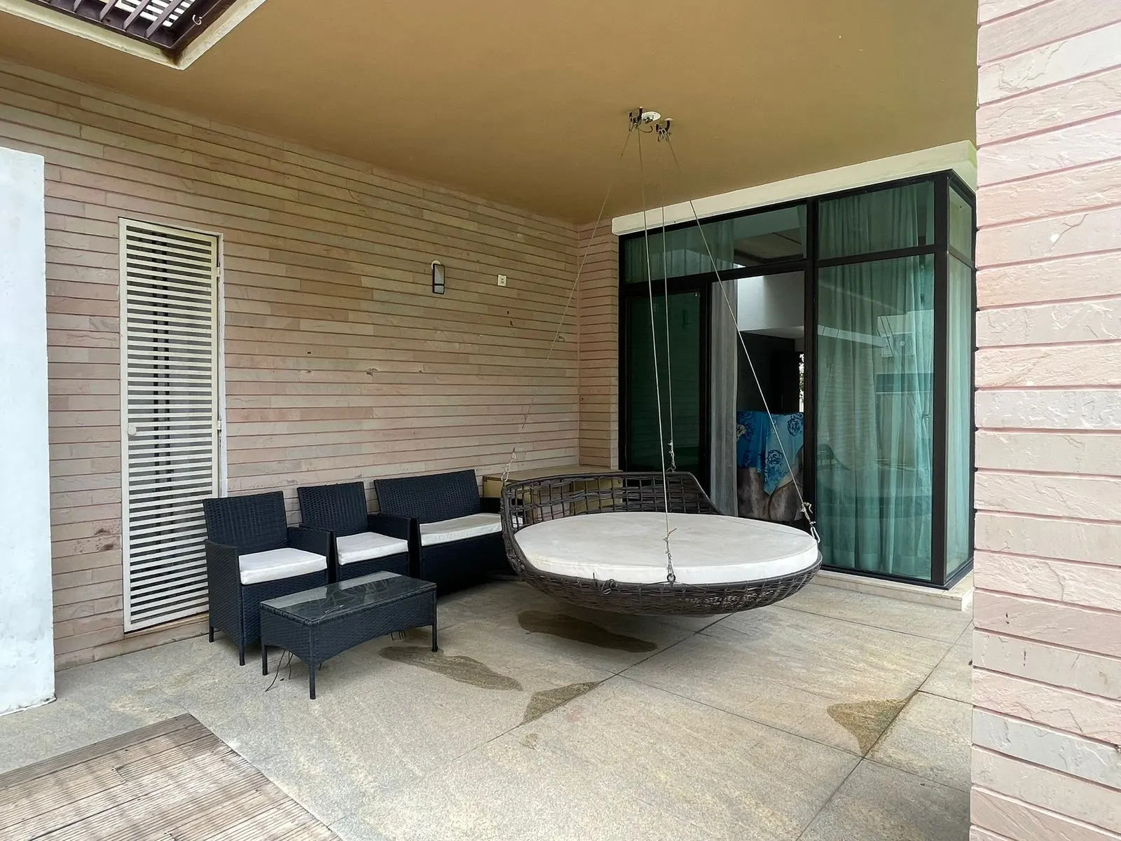 A covered villa patio with a hanging daybed and lounge seating in a Devanahalli gated community