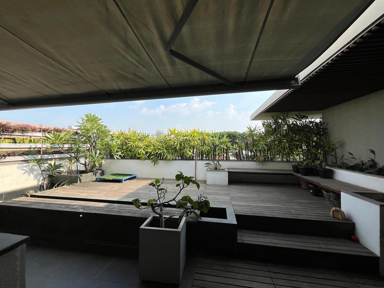 A shaded rooftop terrace with timber decking and potted plants overlooking leafy East Bangalore